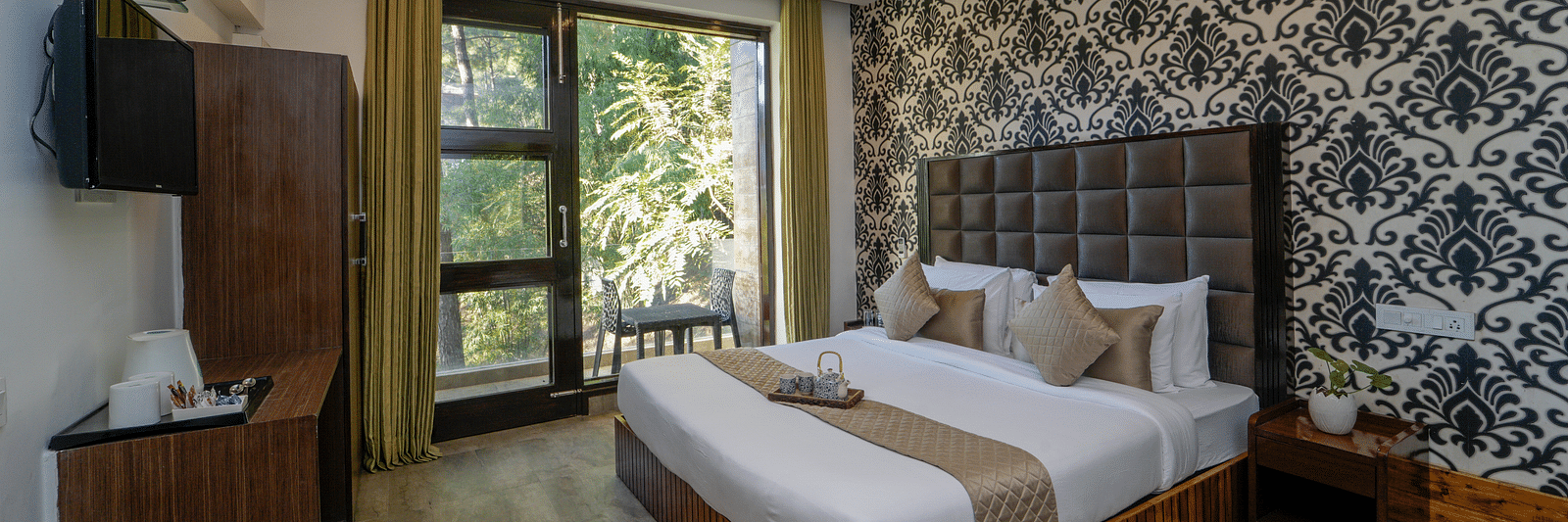 The deluxe room at DLS Whispering Winds featuring a bed, bed side tables, flat screen TV, other room amenities and a glass door leading to the balcony